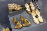 Слева внизу туфли из золотой парчи, декорированные полосками из золотой кожи и чёрного атласа с каблуком Людовик (Великобритания)
